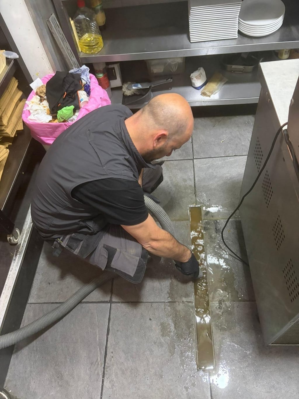 Technicien Nero Canalis nettoyant un caniveau de cuisine professionnelle avec aspirateur en plein centre de Bruxelles